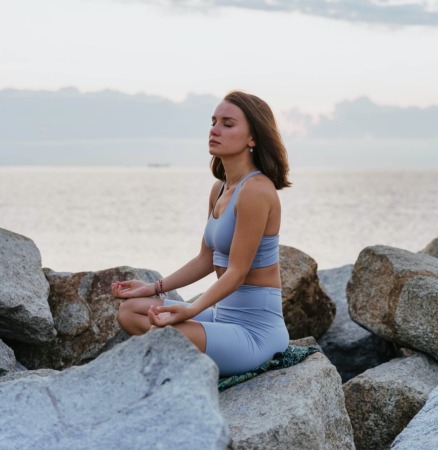Woman practicing a pose of meditation on a beach through Posture Mind and Body Restoration